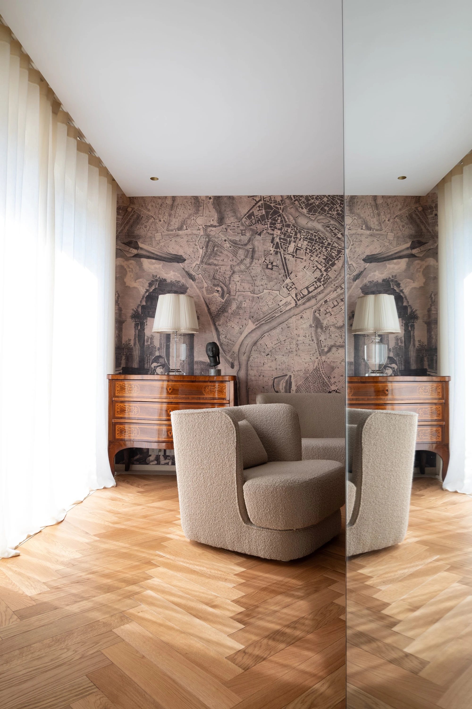 Salotto RN Apartment: poltrona in bouclé sabbia su parquet a spina di pesce, carta da parati custom con riproduzione della piantina di Roma del 1748, comò in legno intarsiato con lampada da tavolo e tende in lino avorio